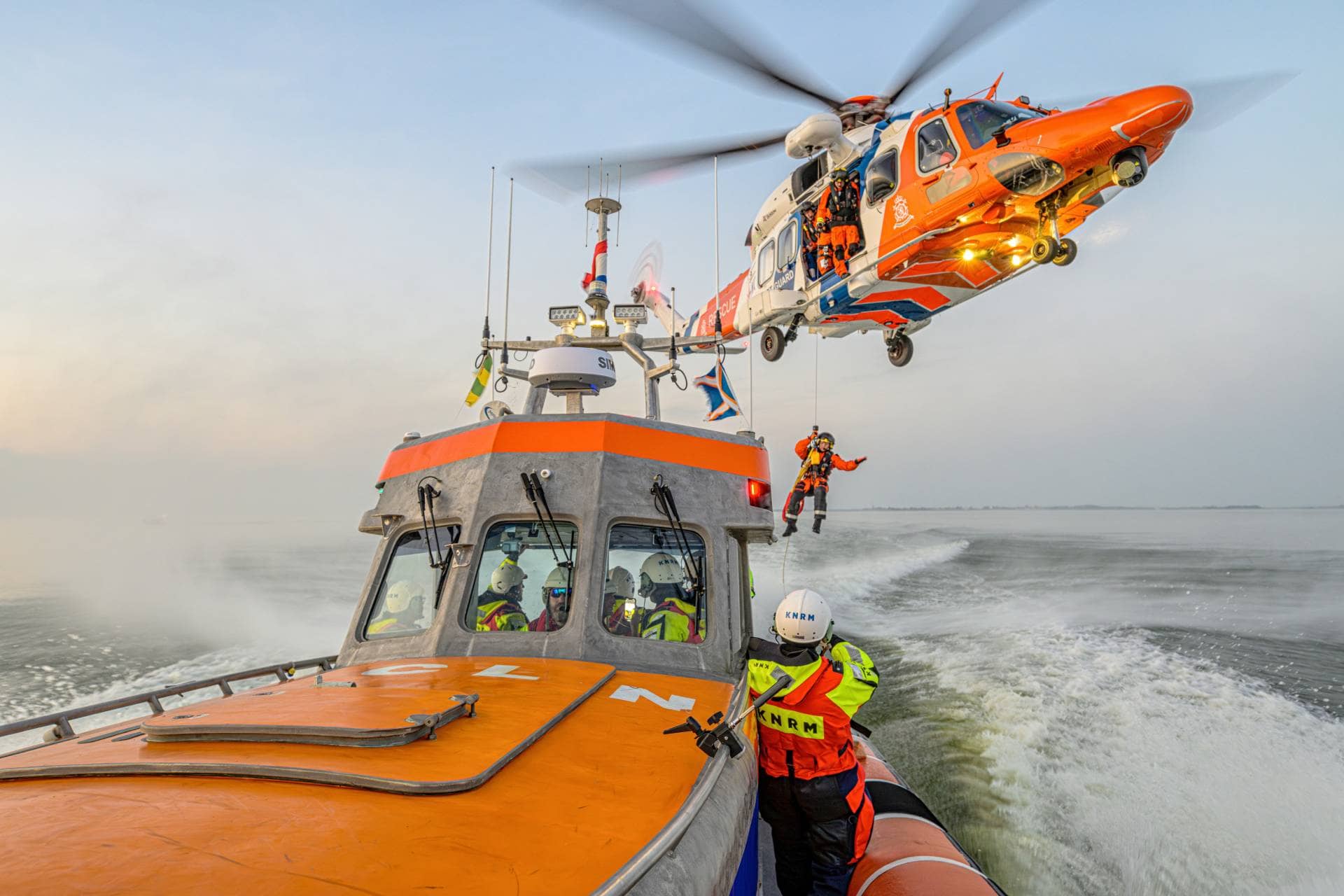 Buque de rescate de la KNRM en el mar con un helicóptero de rescate izando a un miembro de la tripulación