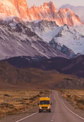 Furgoneta camper amarilla en una carretera abierta bajo el macizo Fitz Roy cubierto de nieve en la Patagonia